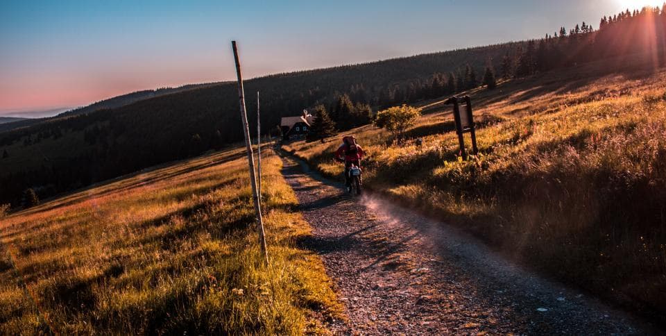 Un motociclista por un camino destapado al atardecer.