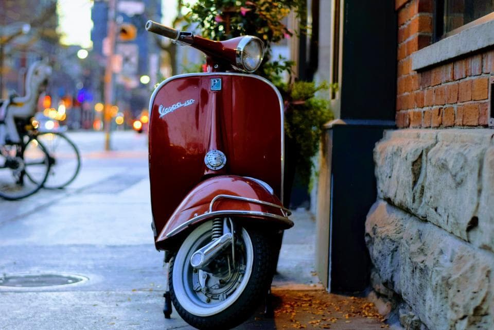 Un scooter rojo parqueado en una calle al atardecer.